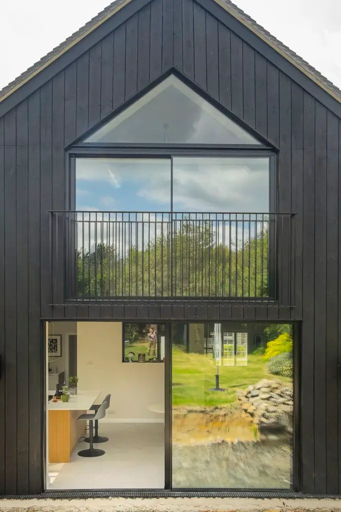 A rear of a modern home, with bespoke glazing, sliding doors and a glass balcony.